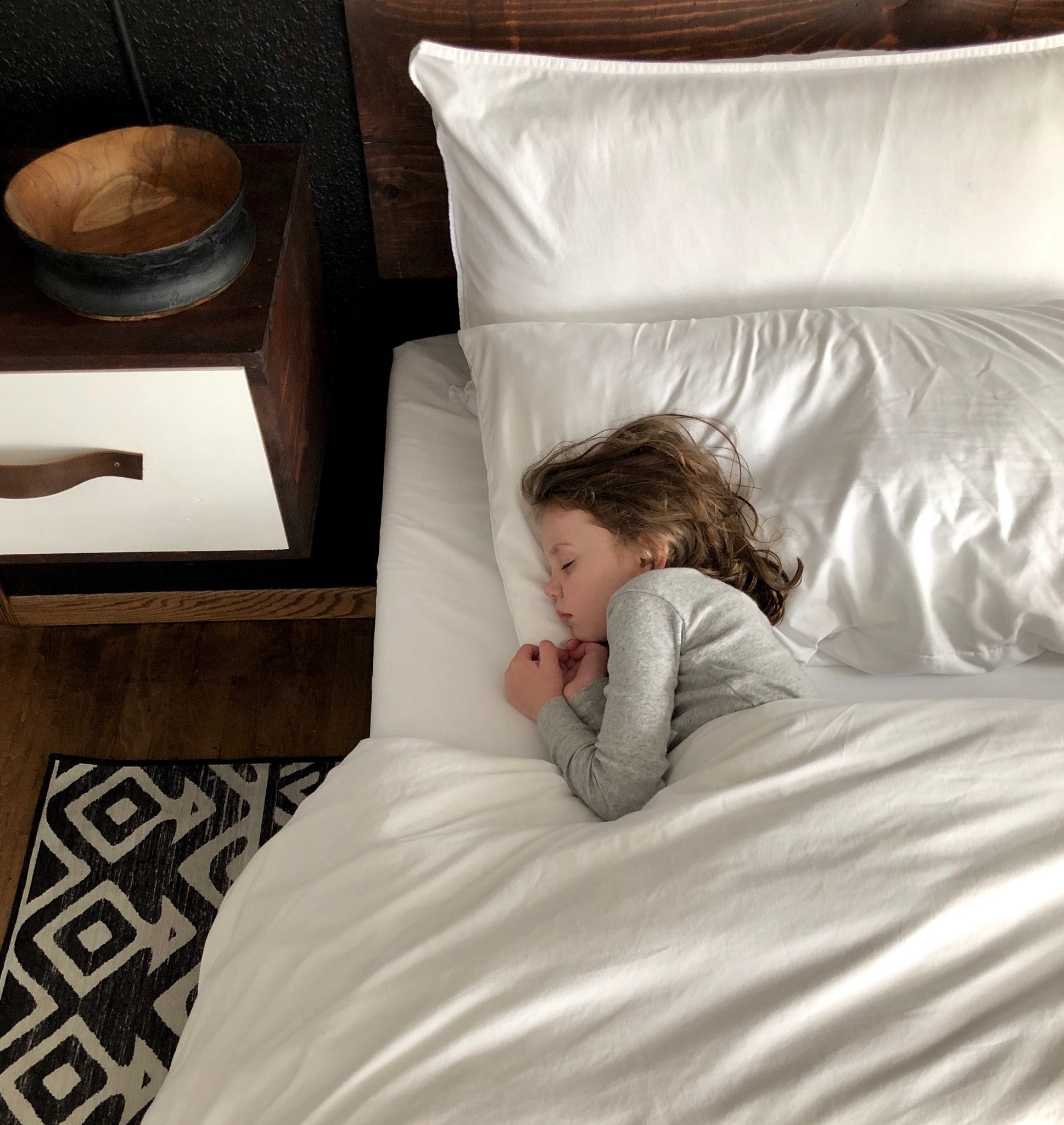 Child peacefully asleep on a neatly made bed with white bedding and wooden headboard, reflecting the comfort and softness of the Zinus mattress for restful sleep.