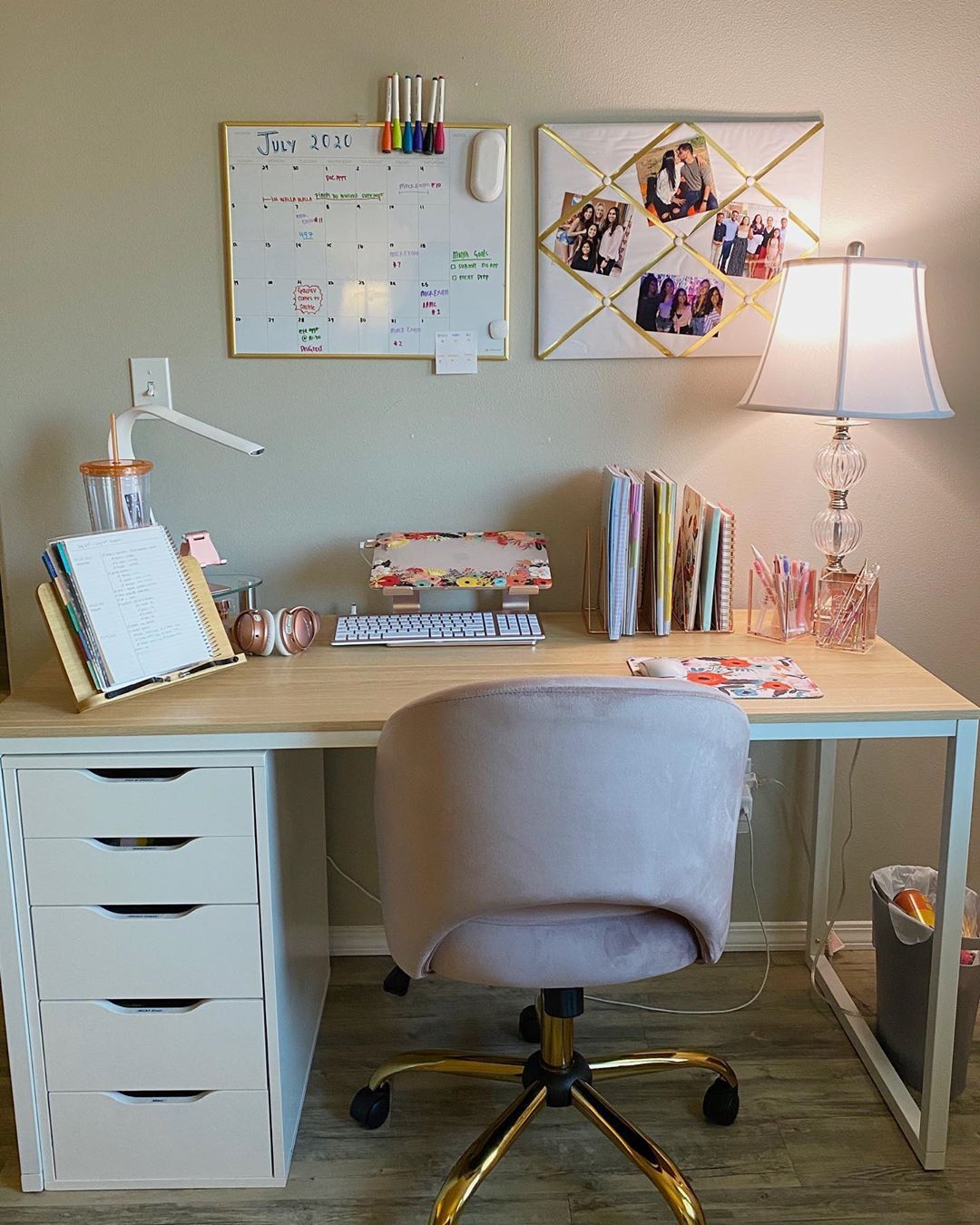 Organized home office with a wooden desk, pink chair, wall calendar, photos, lamp, and neatly arranged stationery.