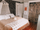 Boho-style bedroom with upholstered bed dressed in warm tan bedding and textured white throw, styled with patterned wallpaper, macramé canopy, and layered pillows to highlight a cozy, eclectic sleep space with inviting comfort and natural accents