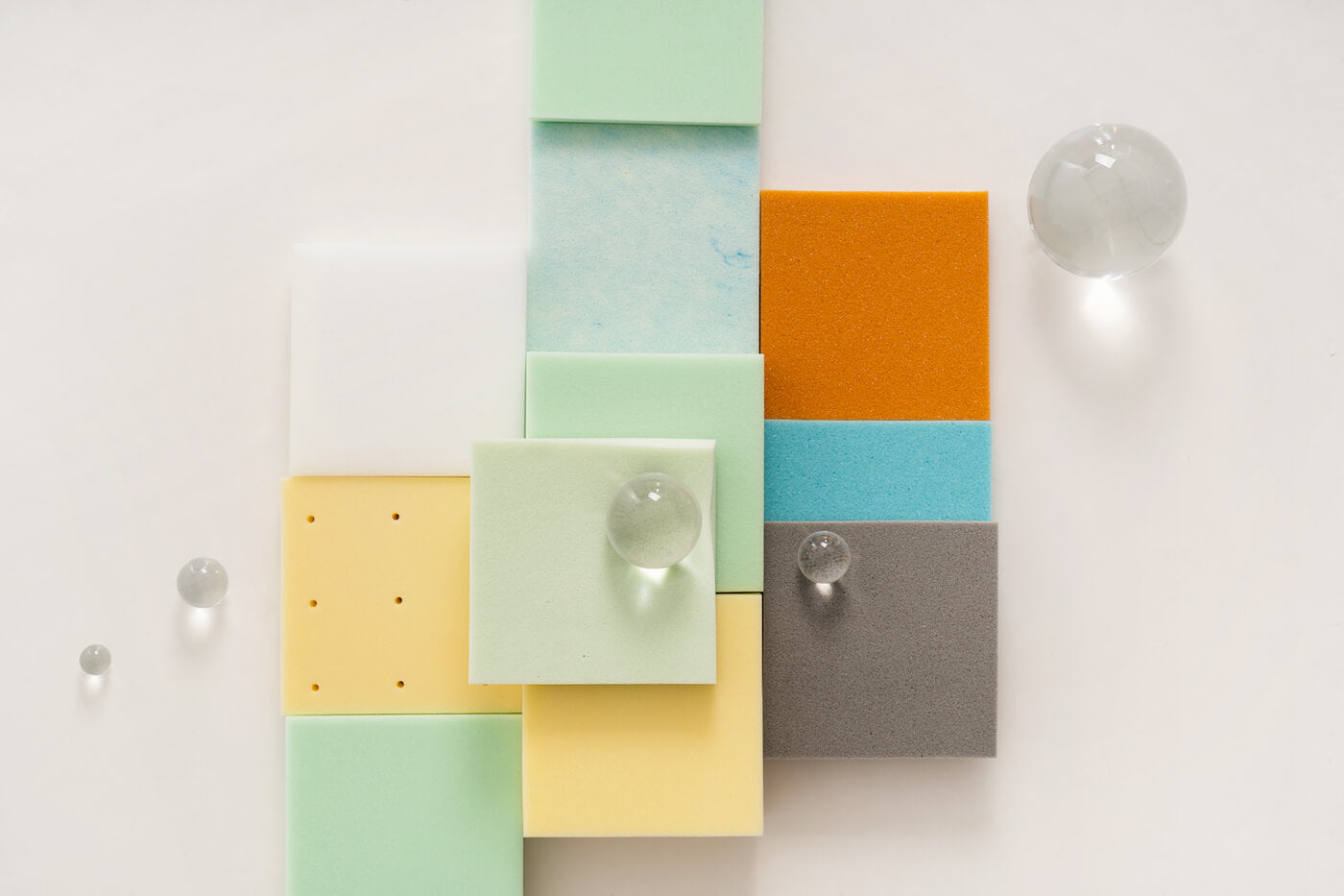 Colorful foam squares arranged in a grid with clear glass spheres placed on top, displayed on a white background