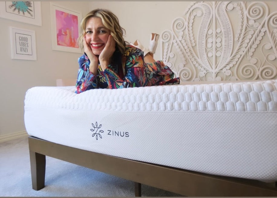 Person lying on a Zinus mattress with a textured white cover, smiling in a bright bedroom with colorful wall art and a decorative headboard