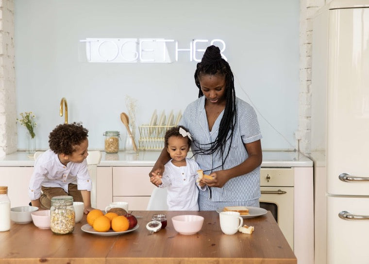 Parent preparing breakfast with two young children at a bright kitchen counter, surrounded by bowls, fruit, and cereal, with a glowing “TOGETHER” sign emphasizing a warm family morning.