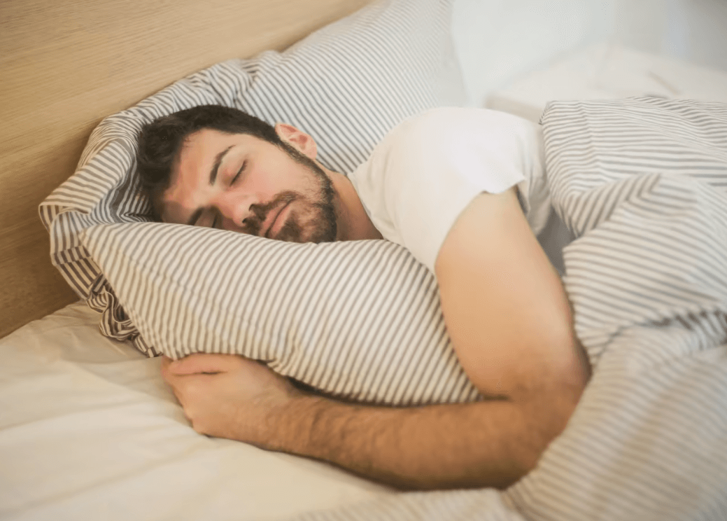 Person sleeping on striped bedding while holding a matching pillow, showing a relaxed nighttime moment in a softly lit bedroom.