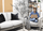 Modern office space with white armchairs, black pillows, shelving with baskets, and a person working on a laptop.