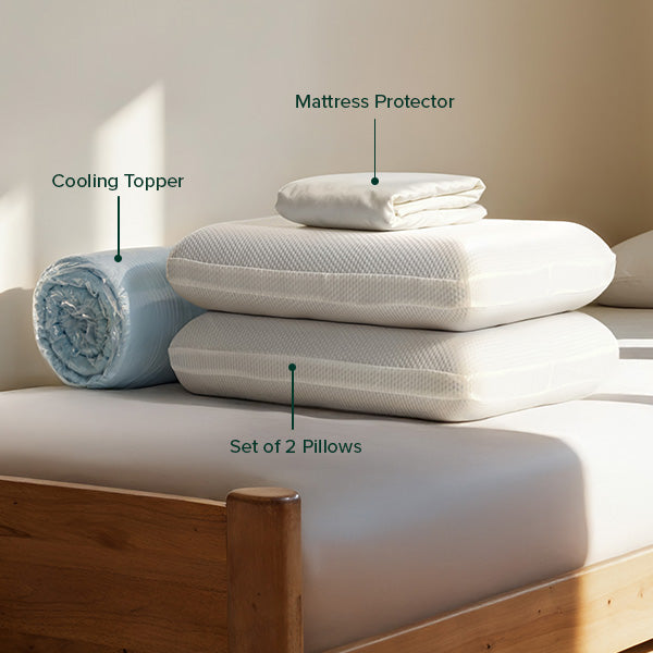 Cooling topper rolled in plastic, a folded mattress protector, and a set of two memory foam pillows neatly arranged on a bed.