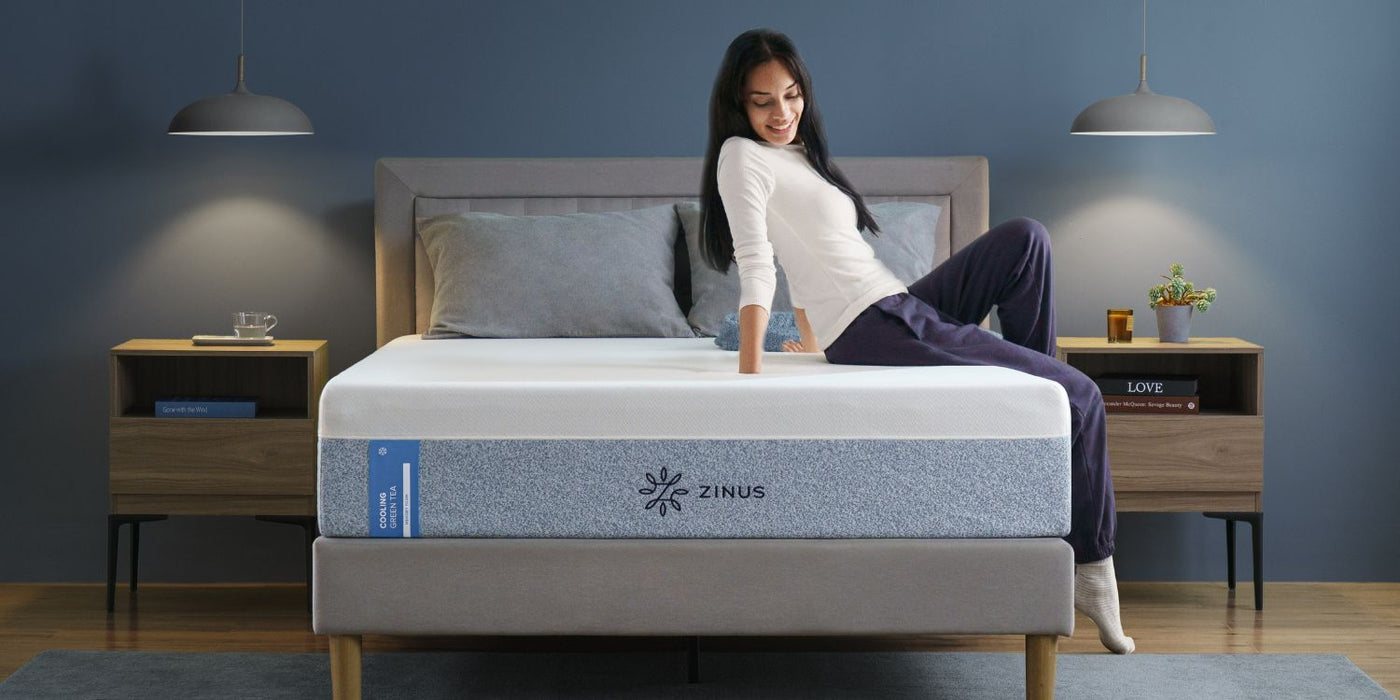 A woman sitting on a Zinus Cooling Green Tea Memory Foam Mattress, featuring cooling gel and pressure relief for better sleep.