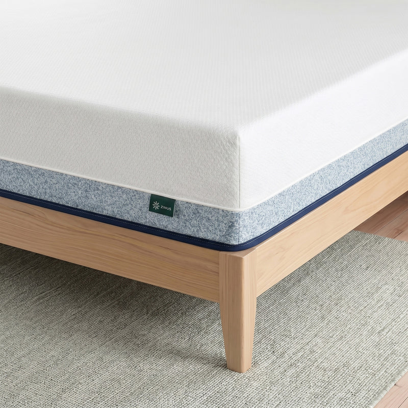Zinus Balanced Comfort Core Hybrid Mattress, close-up corner view showing the white knit top cover, blue woven side panel with navy trim, and Zinus brand tag, set on a natural wood platform bed frame highlighting durable stitching and pocketed coil edge support.