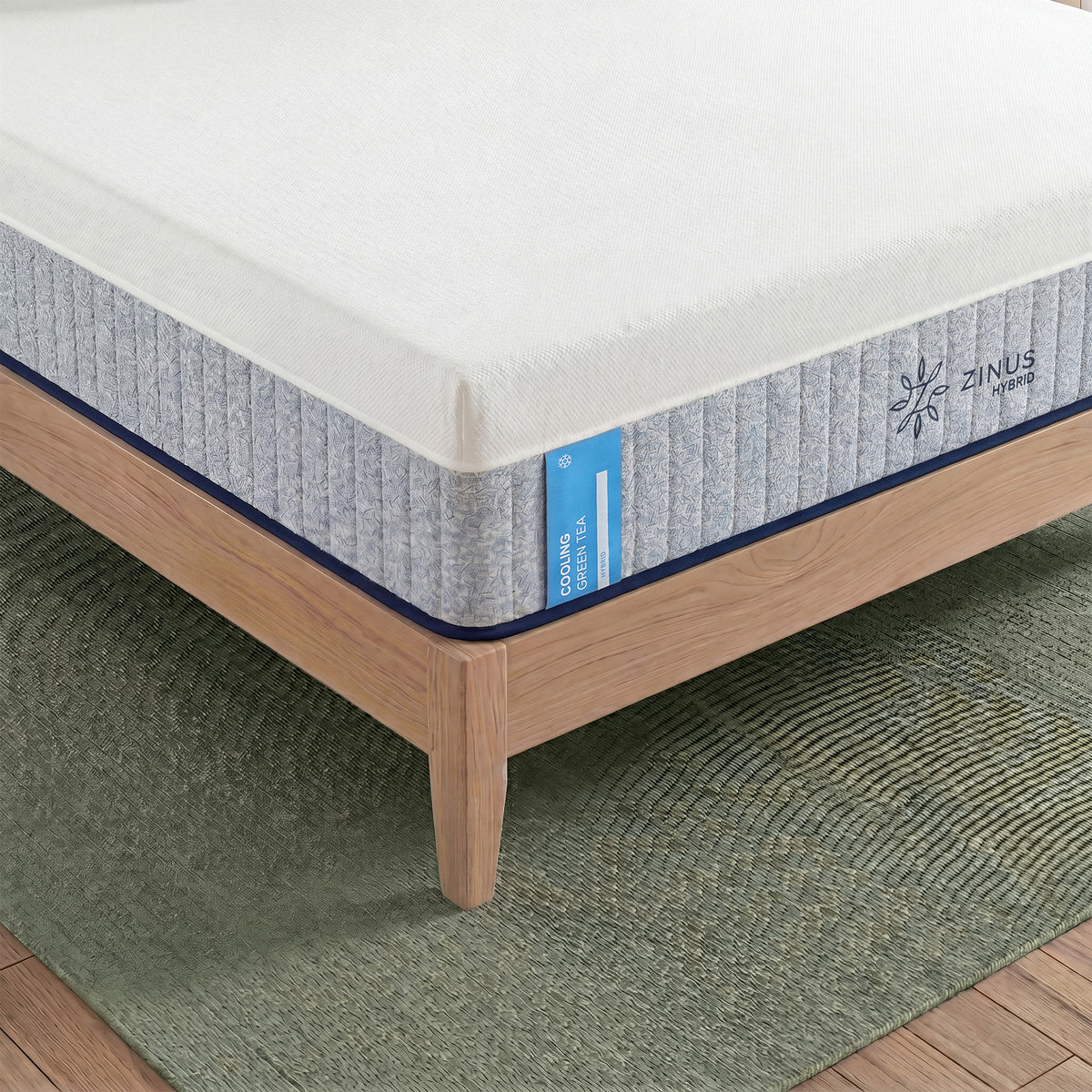 Zinus Balanced Comfort Signature Hybrid Mattress, close-up corner view showing the white knit top cover, channel-quilted gray woven side panel, and Zinus Hybrid brand tag with a cooling icon, set on a natural wood platform bed frame with clean edge stitching.