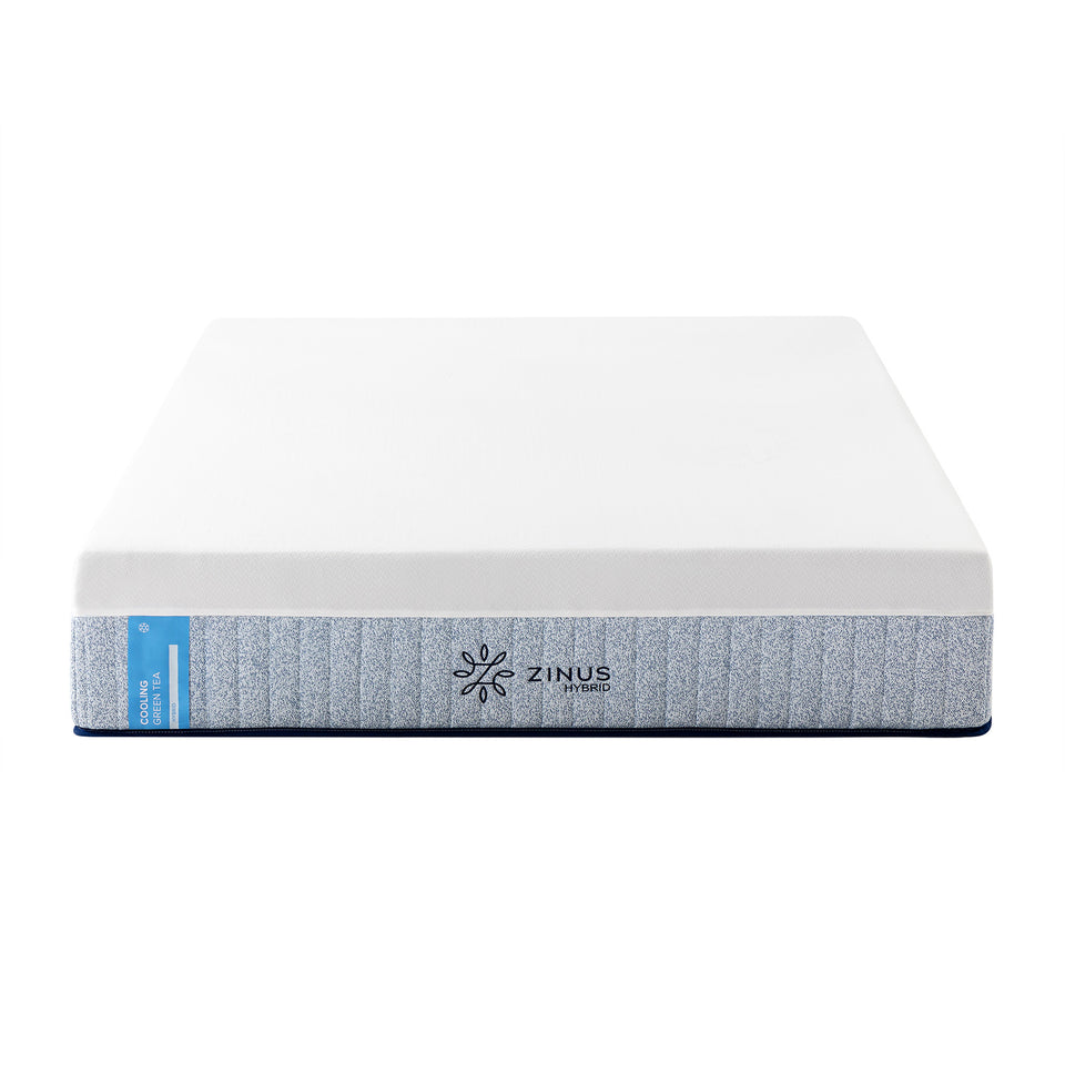 Zinus Balanced Comfort Signature Hybrid Mattress fully set up on a natural wood platform bed with upholstered headboard in a light bedroom with white and green pillows, nightstands, and lamps on either side, showing the mattress in its intended setting.