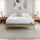 Zinus Balanced Comfort Core Hybrid Mattress fully set up on a natural wood platform bed frame in a light, airy bedroom with white and green pillows, nightstands, and lamps on either side, showing the mattress in its intended home bedroom setting.