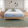 Zinus Balanced Comfort Signature Hybrid Mattress fully set up on a natural wood platform bed with upholstered headboard in a light bedroom with white and green pillows, nightstands, and lamps on either side, showing the mattress in its intended setting.
