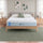 Zinus Balanced Comfort Signature Memory Foam Mattress fully set up on a natural wood platform bed with upholstered headboard in a light bedroom with white and green pillows, nightstands, and lamps on either side, showing the mattress in its intended setting.