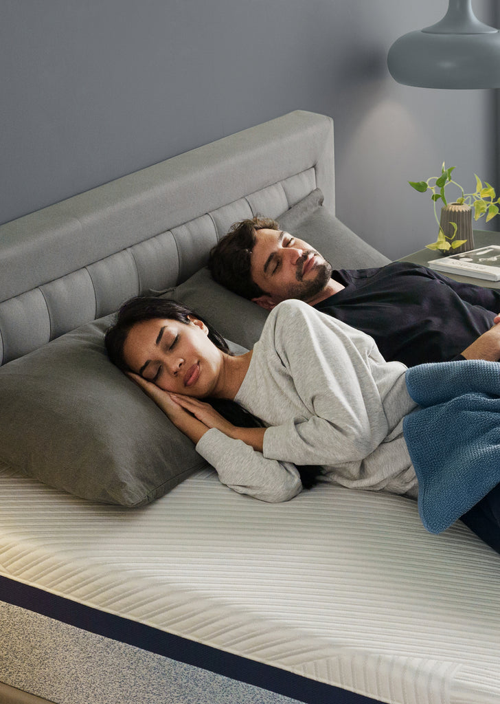 Woman in cozy white top hugs a Zinus Ultra Cooling Green Tea mattress, smiling peacefully. Bedroom setting features modern décor and gray upholstered frame. Image emphasizes mattress comfort, cooling memory foam, and deep relaxation benefits 