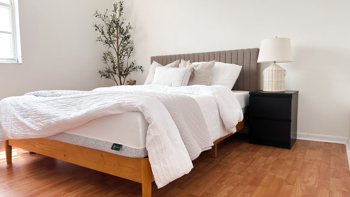 Zinus mattress with white top and speckled gray side panel on wood platform bed frame, styled with neutral pillows, white quilt, and fluted beige headboard in a bright bedroom with wood floors, black nightstand, and decorative lamp, highlighting clean modern style