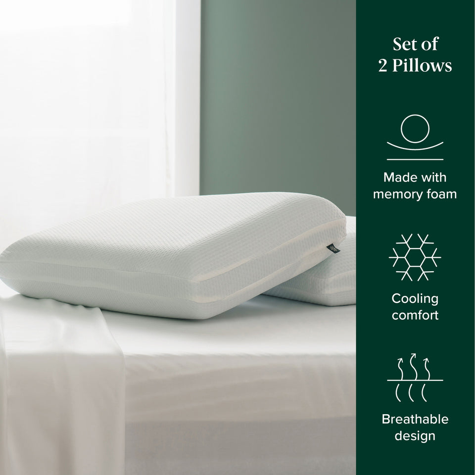 Two white memory foam pillows with breathable covers stacked on a neatly made bed, styled beside window. On-screen text highlights features: memory foam, cooling comfort, breathable design.
