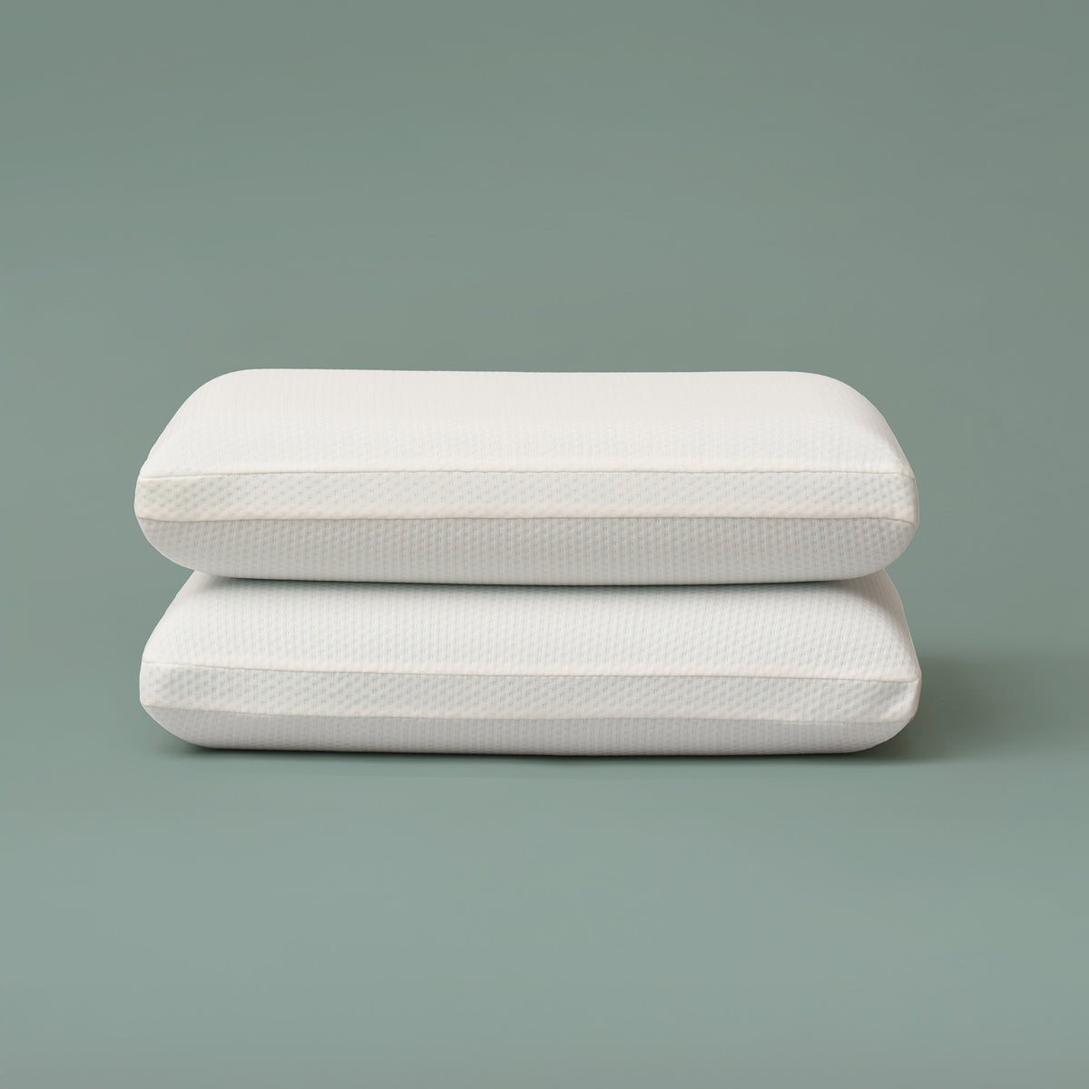 Set of two rectangular cooling memory foam pillows stacked against a muted green background, featuring smooth white breathable knit covers and supportive shape designed for comfort and temperature regulation during sleep