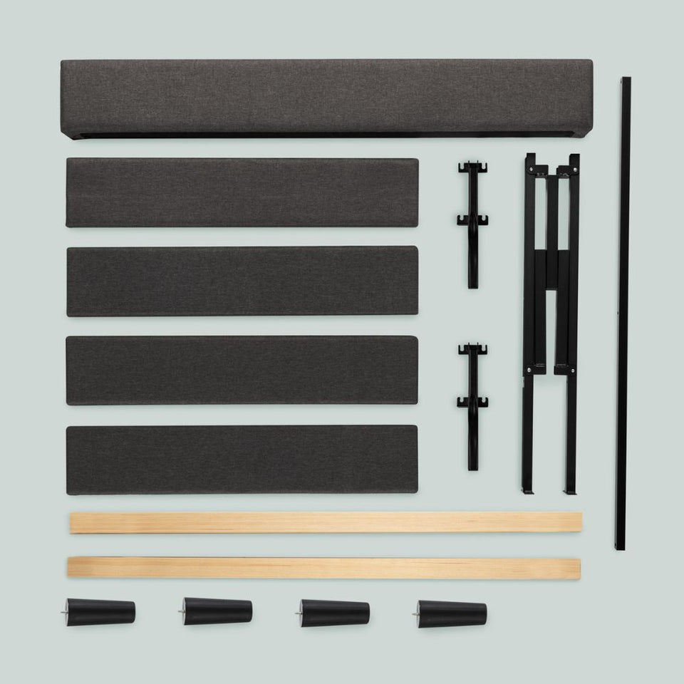 Unassembled upholstered bed frame components laid out, including tufted headboard, side rails, support legs, center frame pieces, wood slats, and tapered wood legs, all ready for tool-free assembly.