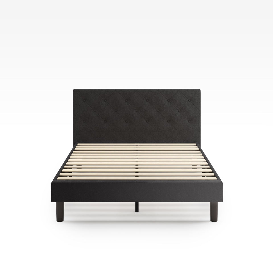 Zinus Shalini Upholstered Platform Bed Frame in a dark gray finish, shown from the front without a mattress. Features a button-tufted headboard, wooden slats for strong mattress support, and a modern upholstered design that fits any bedroom style