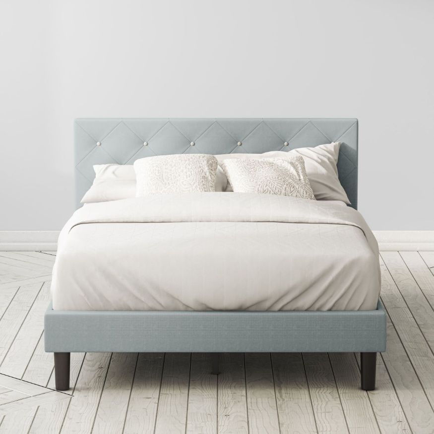 Zinus Shalini Upholstered Platform Bed Frame styled with white bedding in a minimal bedroom. The diamond-stitched headboard in dark gray fabric adds sophistication, while durable slats provide strong mattress support without the need for a box spring